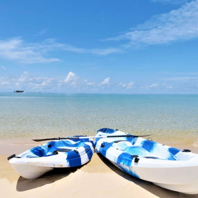 Two blue and white kayaks on a sandy beach with clear blue water and sky.